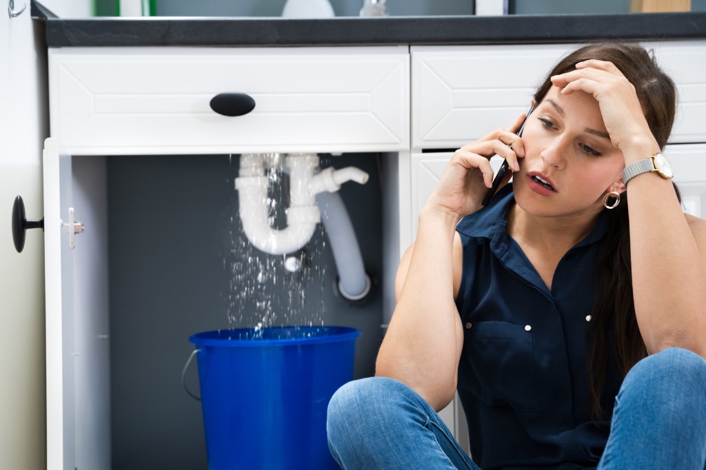 Plumber repairing a pipe leak under a sink